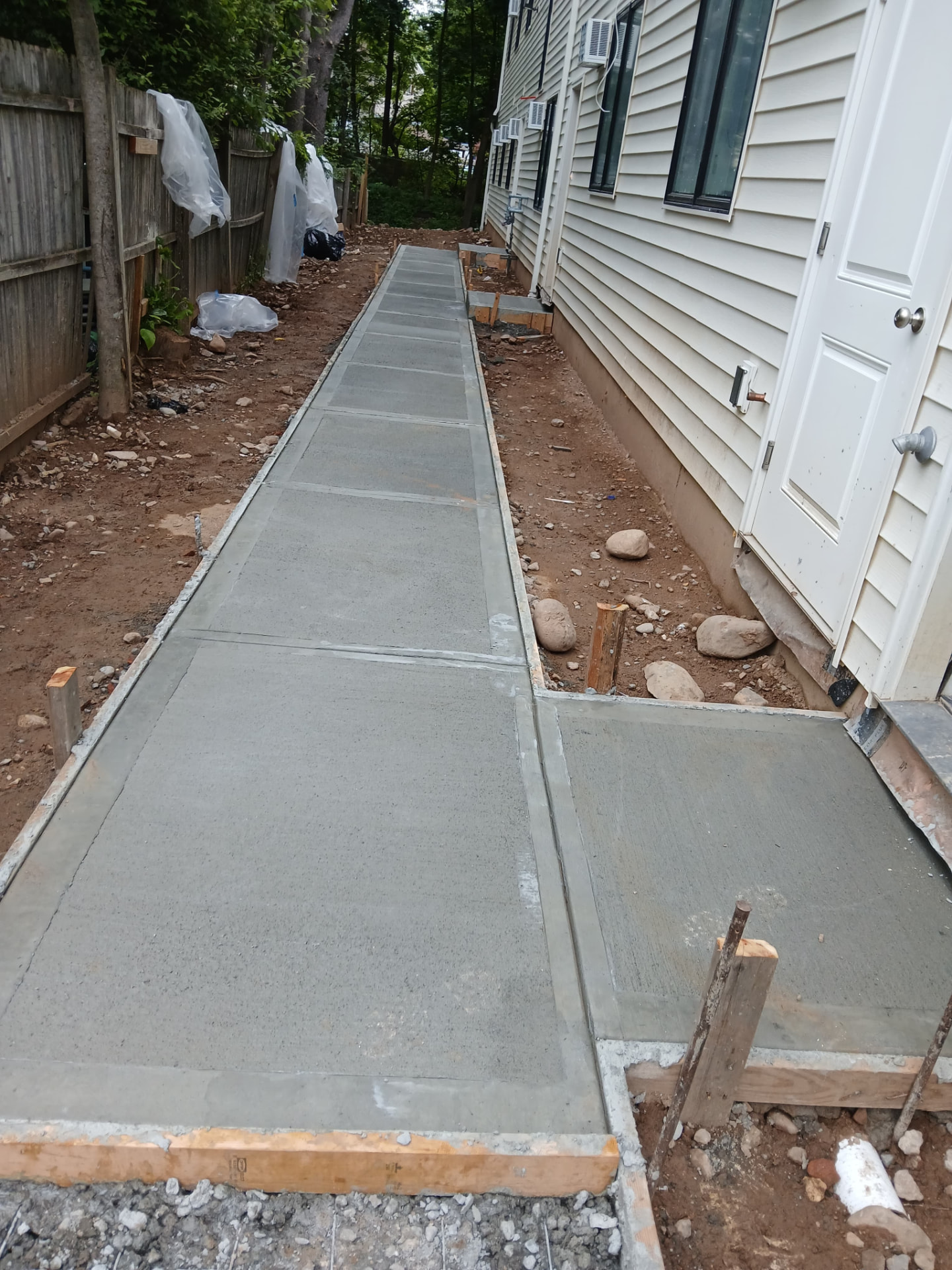 Newly finished concrete sidewalk with formed control joints alongside a house