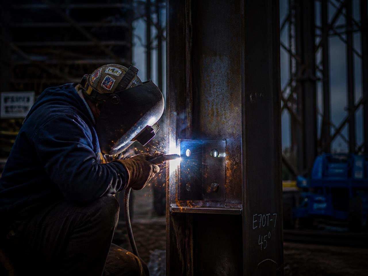 Welder joining a steel bracket to a structural beam on a construction site
